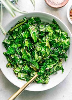 a bowl of sautéed collard leaves on a white table with a gold fork