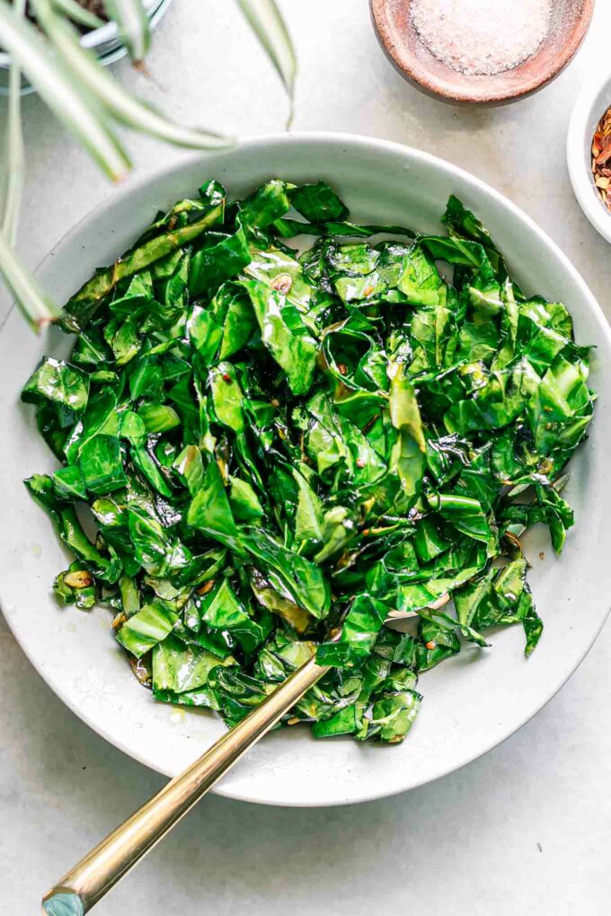 a bowl of sautéed collard leaves on a white table with a gold fork