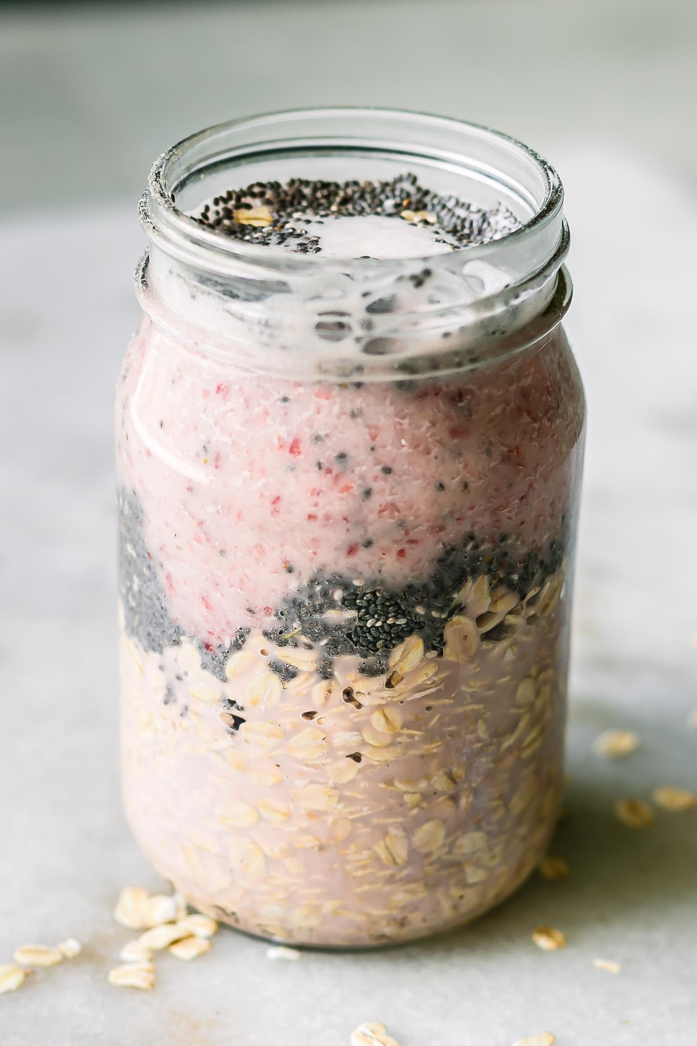 a jar with rolled oats, chia seeds, and strawberry milk for overnight oats on a white table