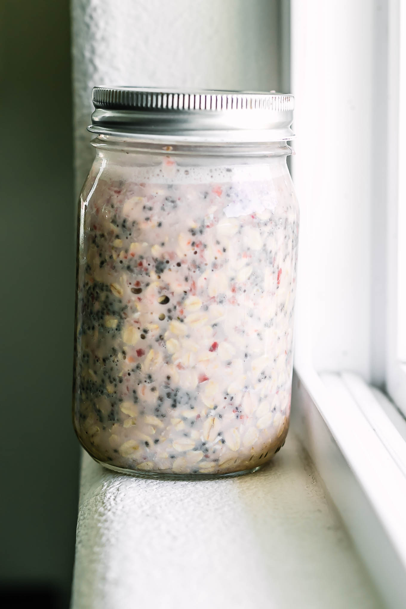 a small mason jar with strawberry overnight oat ingredients on a white windowsill