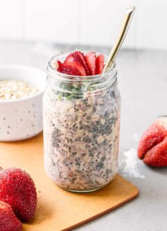 a jar of overnight oats with strawberries on a wood table with fresh strawberries