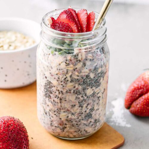 a jar of overnight oats with strawberries on a wood table with fresh strawberries