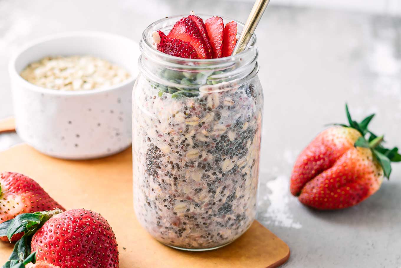 a jar of overnight oats with strawberries on a wood table with fresh strawberries