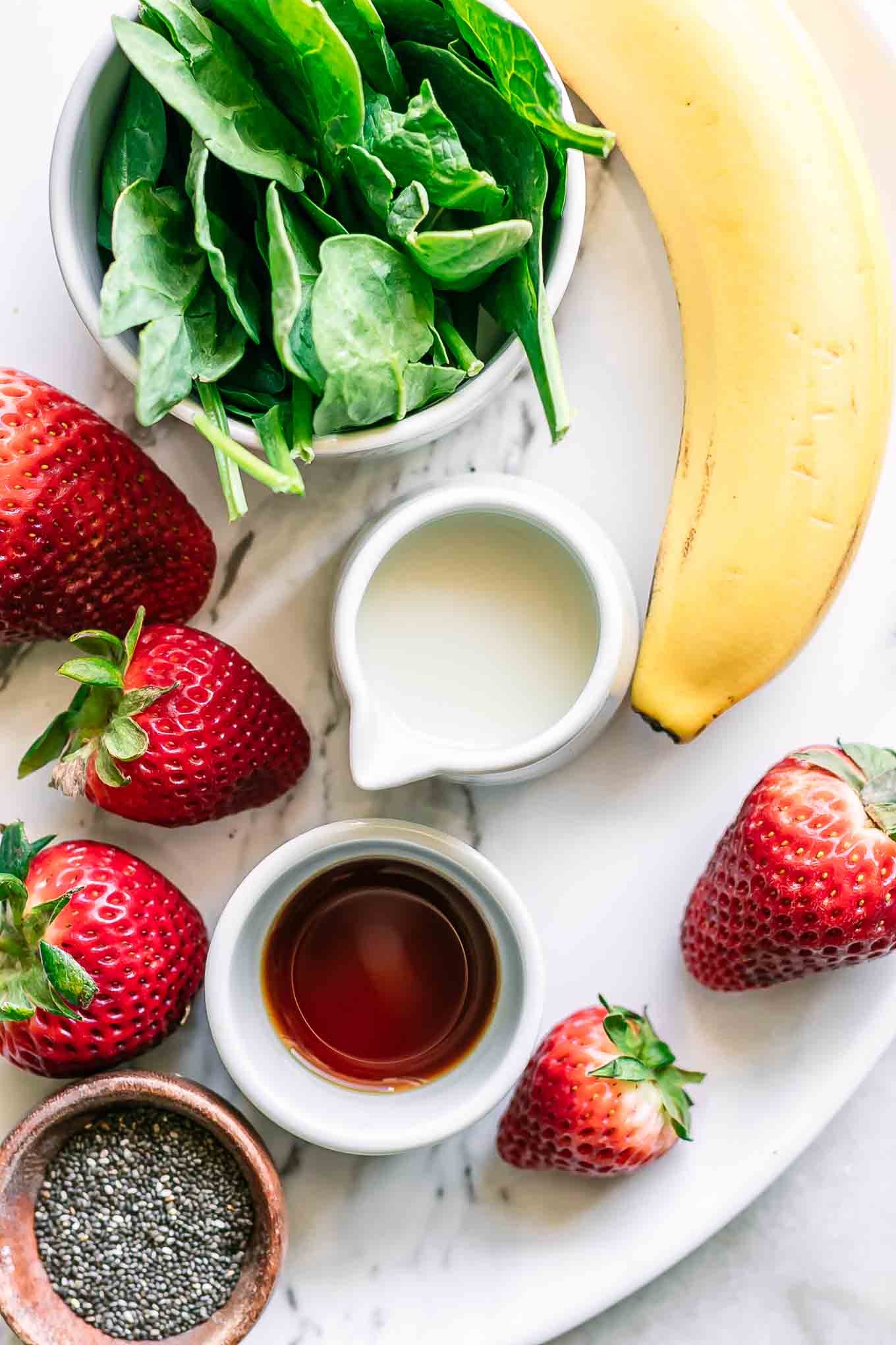 strawberries, spinach, banana, chia seeds, milk, and vanilla on a table for a smoothie