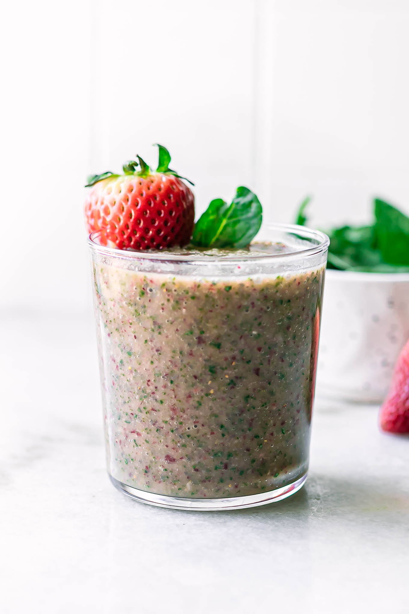 a glass with a spinach smoothie with strawberries on a white countertop