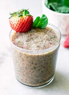 a smoothie with strawberries and spinach in a glass on a white table