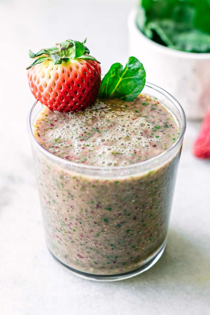 a smoothie with strawberries and spinach in a glass on a white table