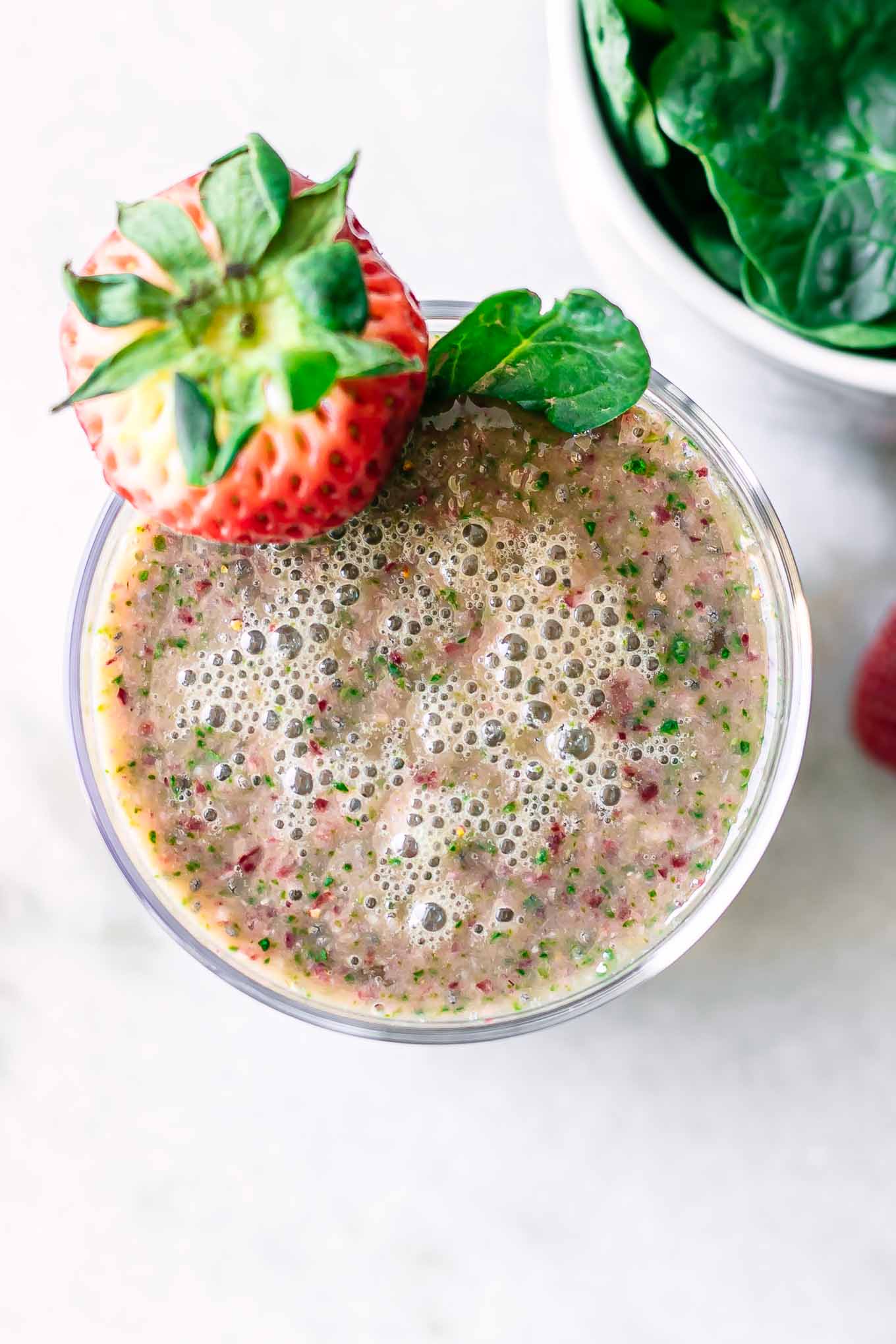 a close up photo of the top of a spinach strawberry smoothie in a glass with a strawberry garnish