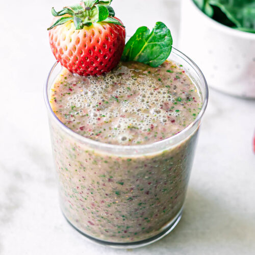 a glass with strawberry spinach smoothie with a strawberry garnish on a white table