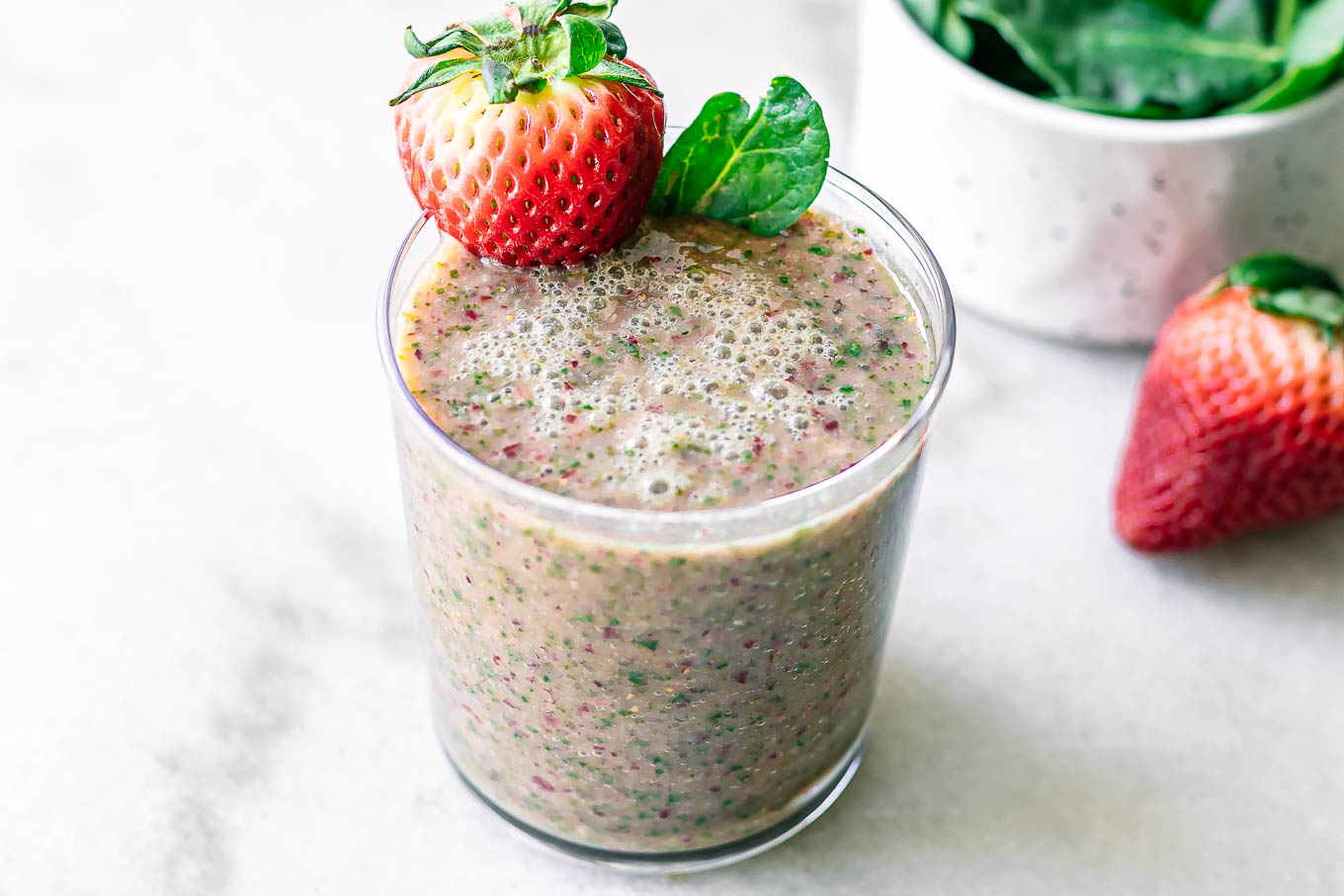 a glass with strawberry spinach smoothie with a strawberry garnish on a white table