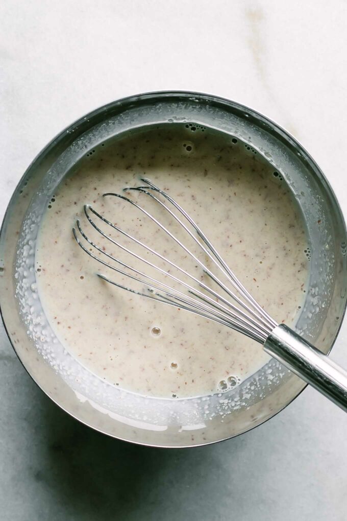 a small mixing bowl with liquid ingredients for bran muffins with a whisk on a white table
