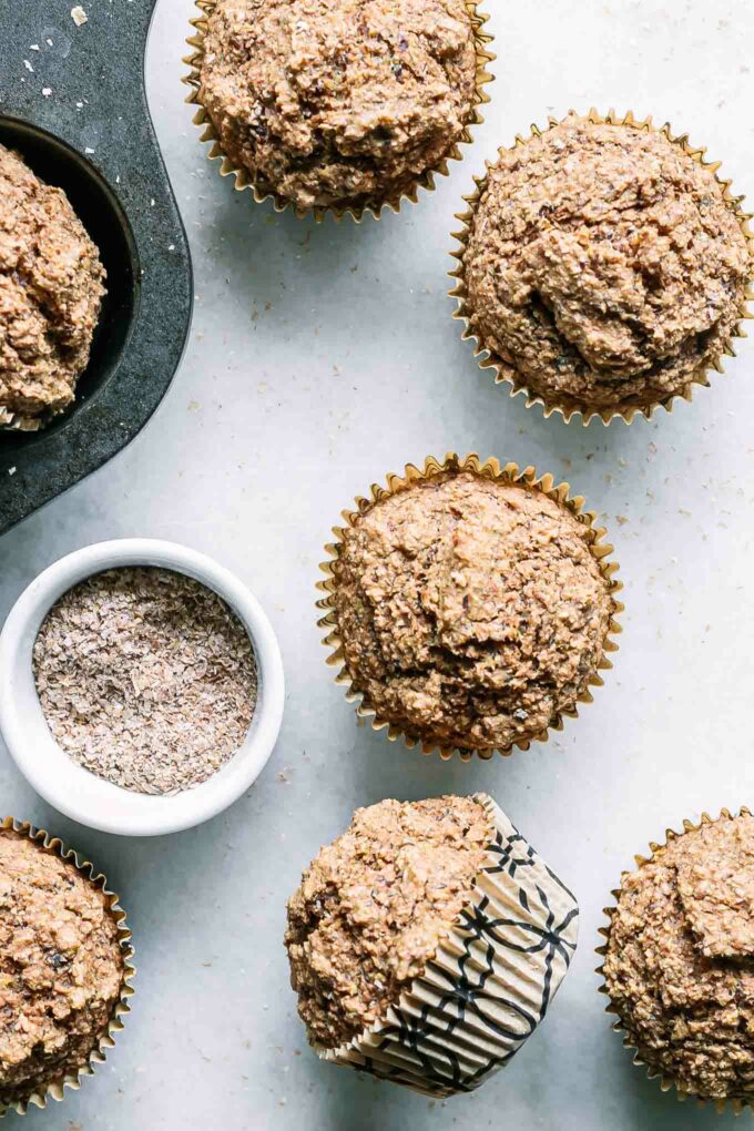 vegan bran muffins on a white table with a bowl of wheat bran