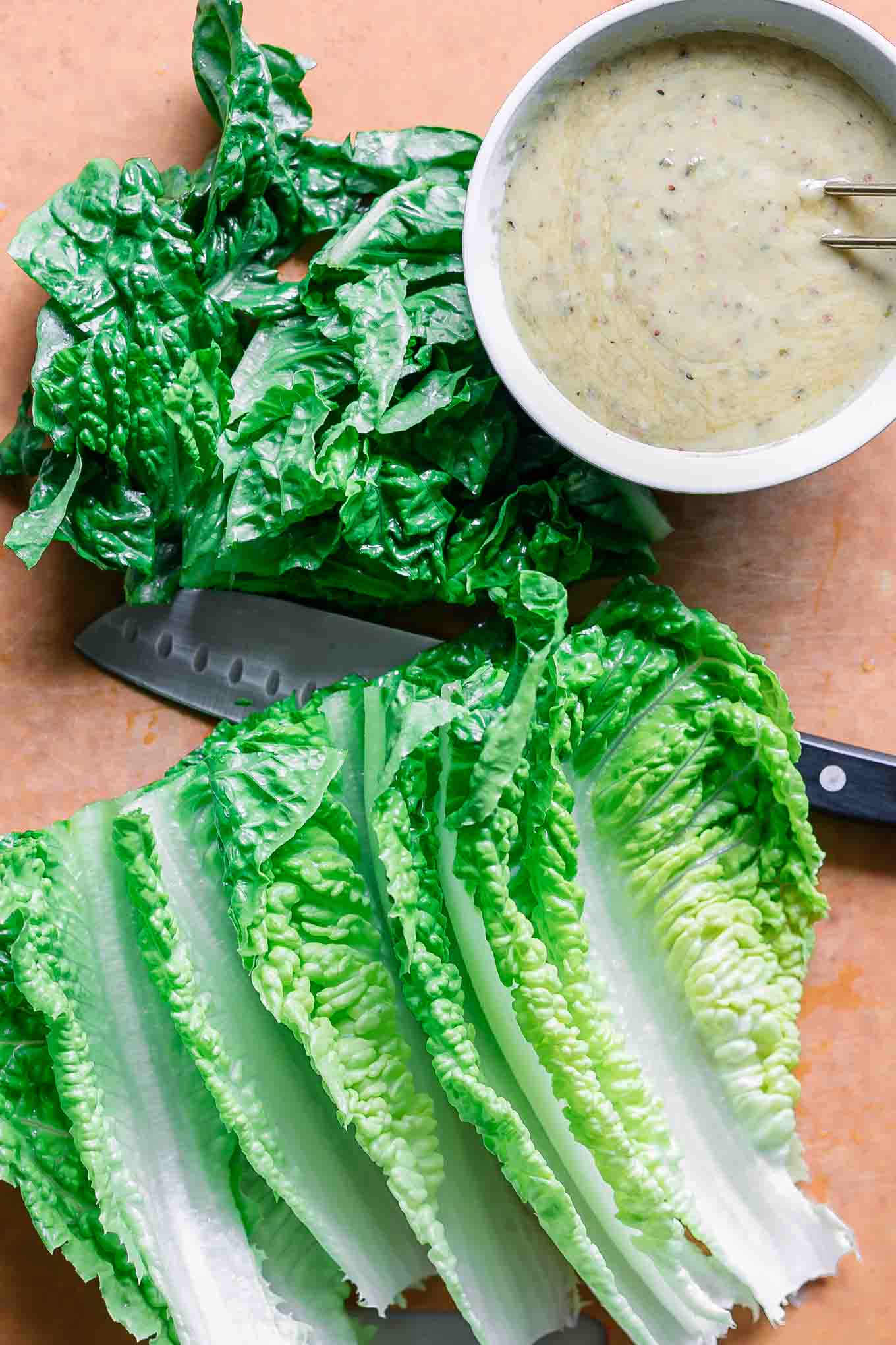 cut romaine lettuce on a cutting board with a bowl of caesar dressing