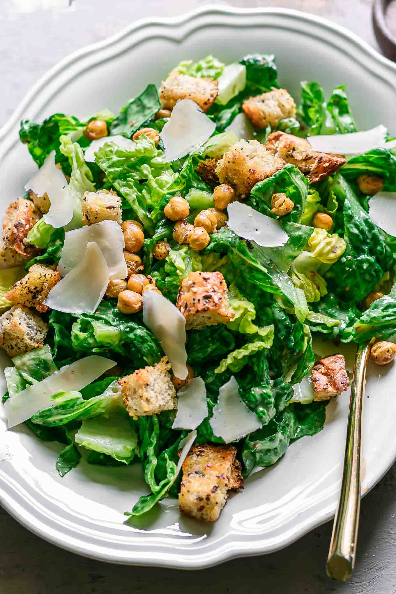 a plant-based caesar salad on a white plate with a gold fork