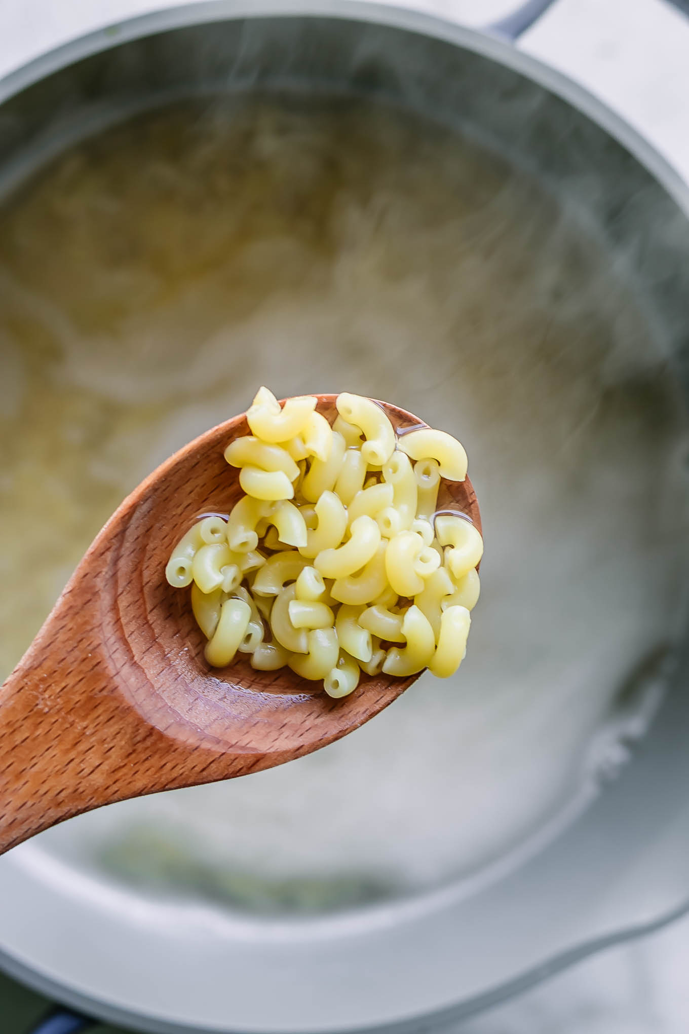 a pot of boiling water with a wooden spoon with elbow macaroni pasta