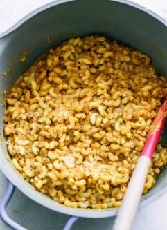 a large pot with plant-based sweet potato macaroni and cheese with a wood spoon