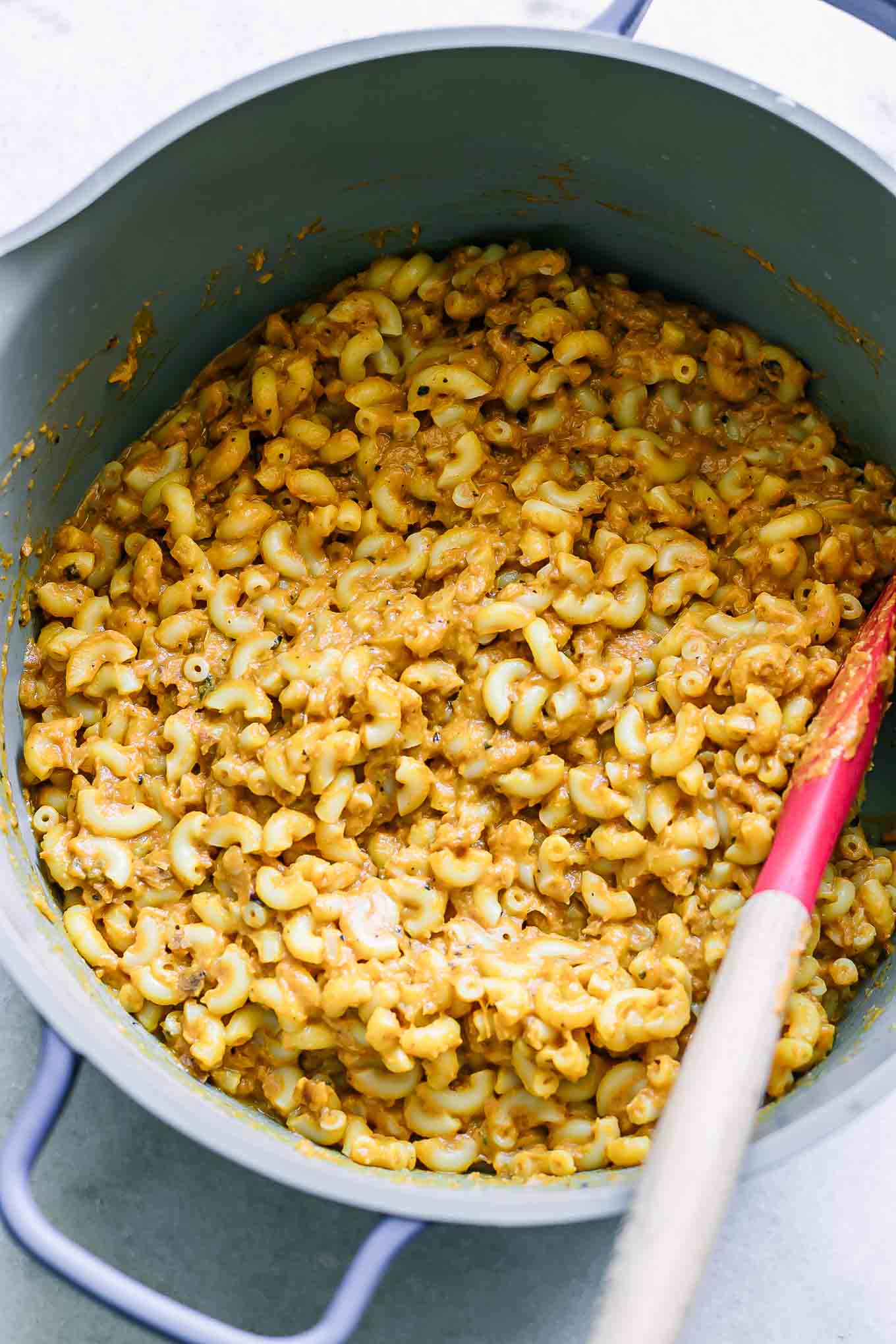 a large pot with plant-based sweet potato macaroni and cheese with a wood spoon