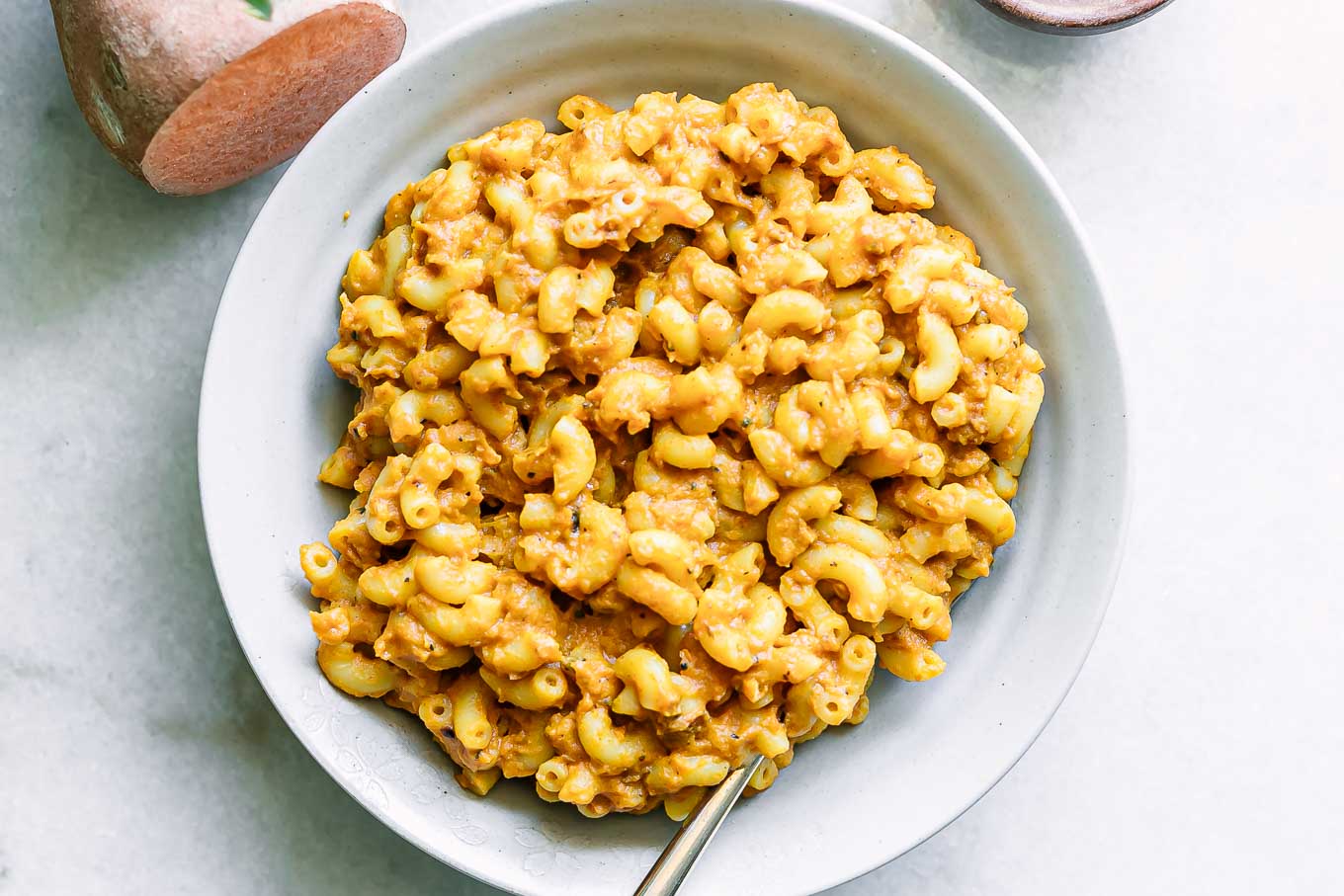 a white plate with sweet potato macaroni and cheese with a gold fork