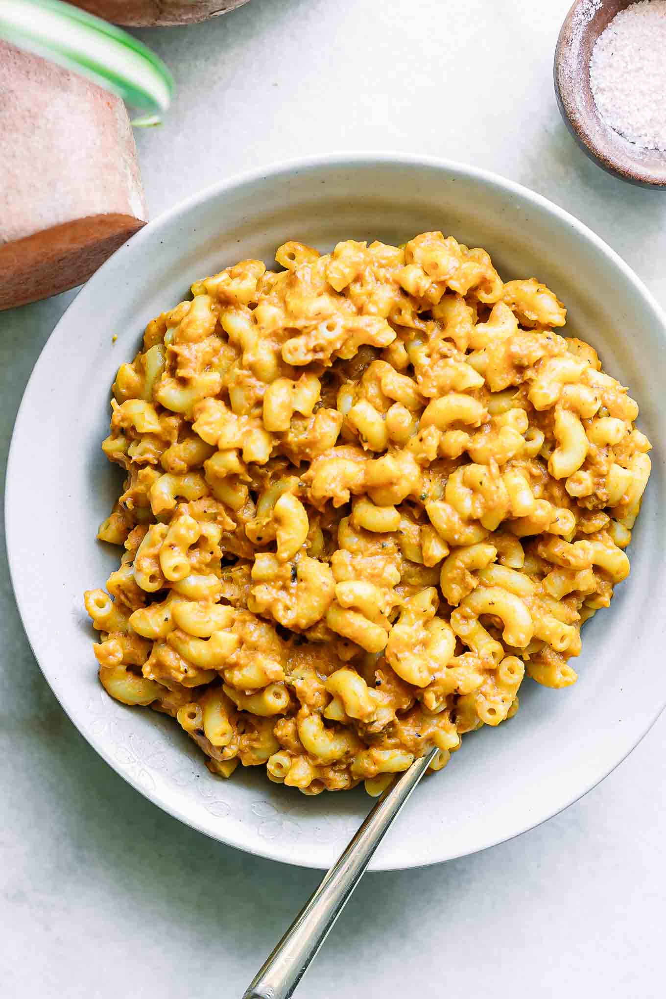 a bowl with sweet potato macaroni and cheese with a gold fork on a white table