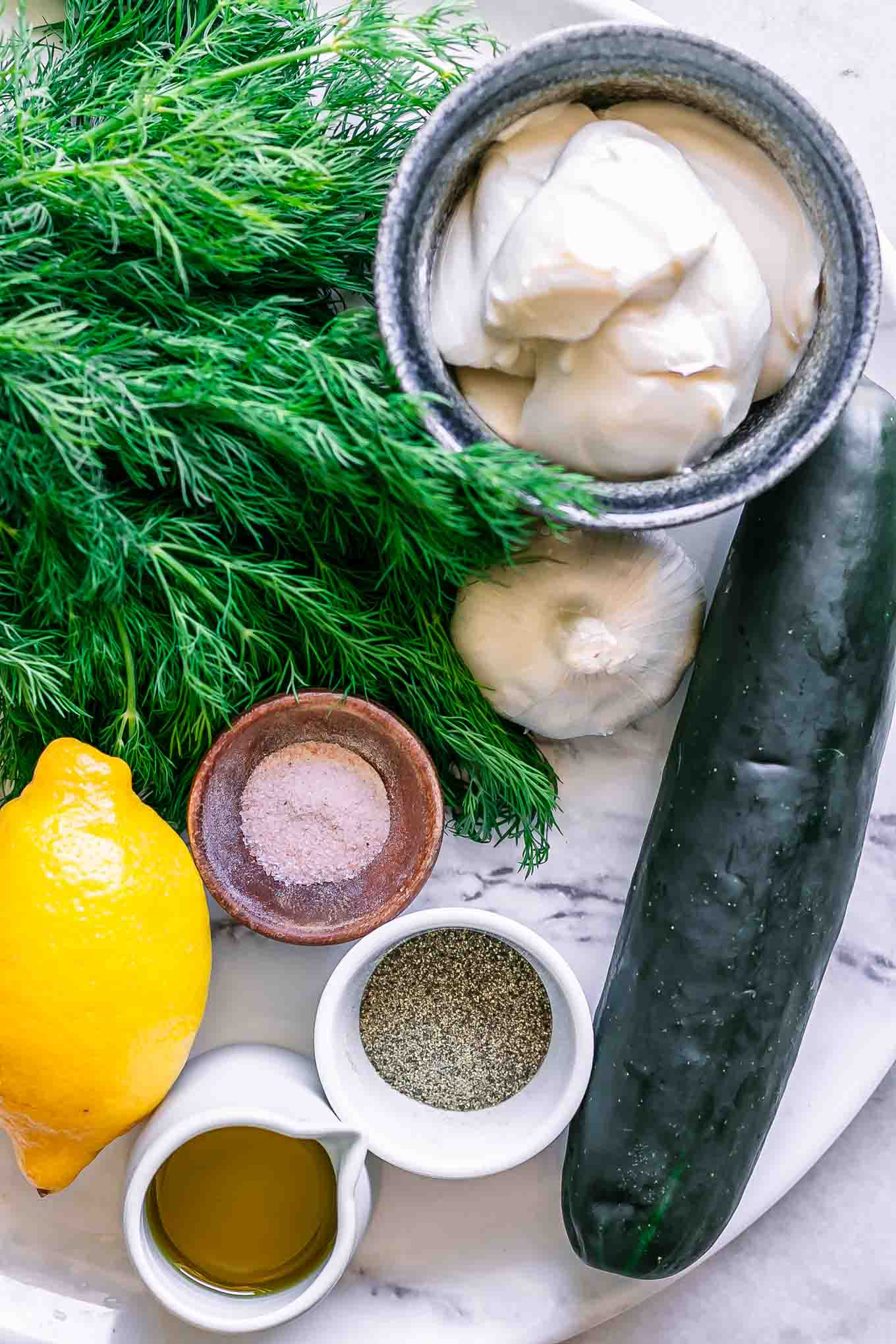 a cucumber, fresh dill, vegan yogurt, lemon, garlic, and spices on a table for vegan tzatziki sauce