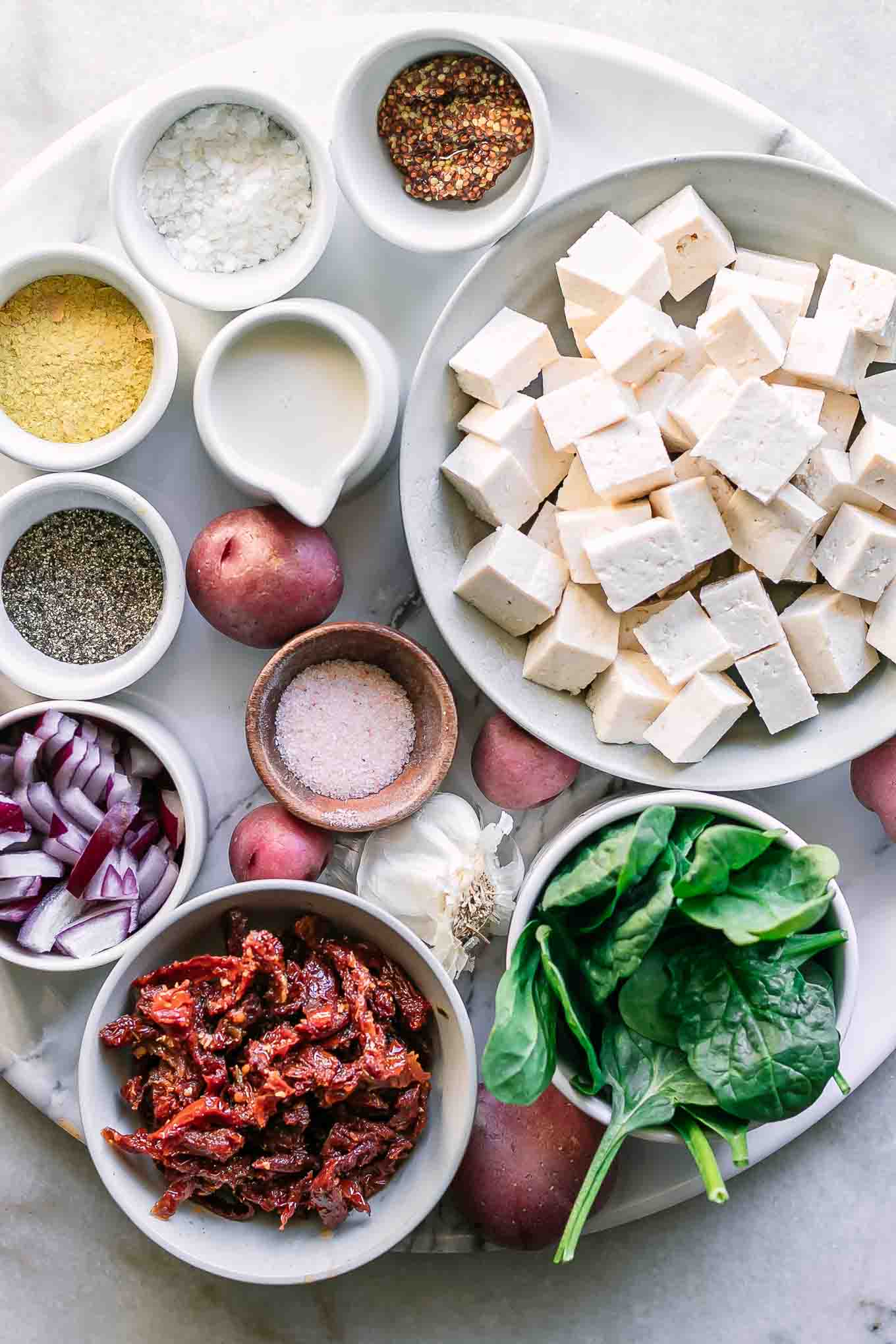 bowls of tofu, vegetables, and seasonings on a white table for a vegan frittata