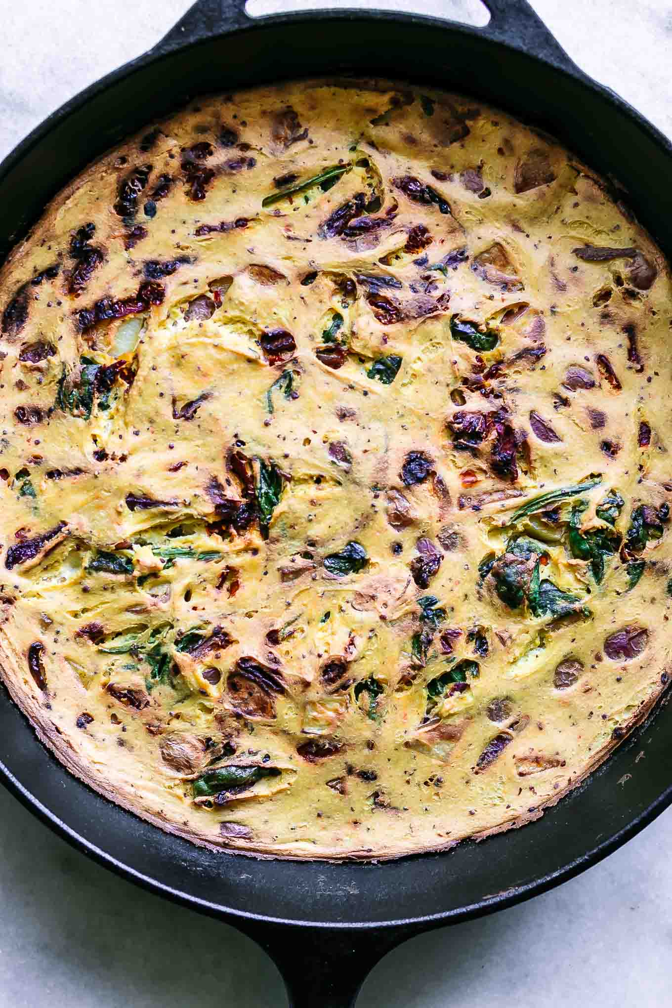 a cooked tofu frittata in a cast iron skillet on a white table
