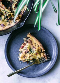 a blue plate with a slice of vegan tofu frittata with a gold fork on a white table