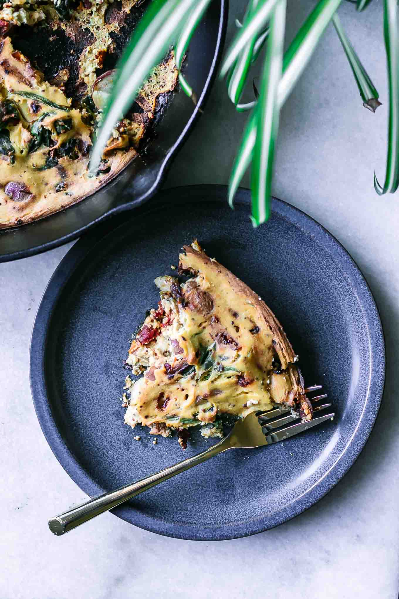 a blue plate with a slice of vegan tofu frittata with a gold fork on a white table