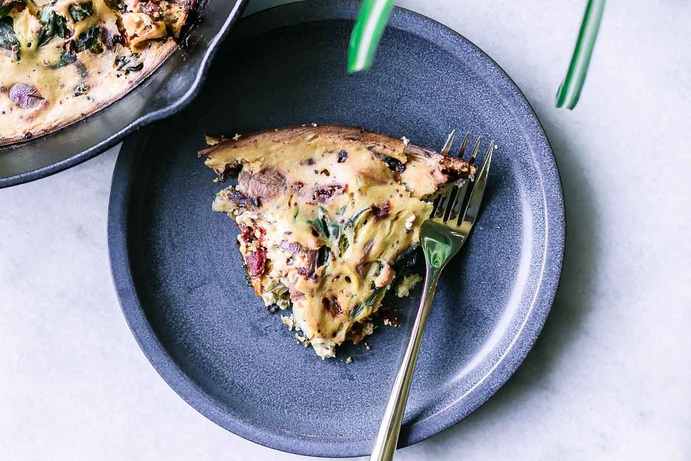 a blue plate with a slice of vegan vegetable frittata with a gold fork on a white table