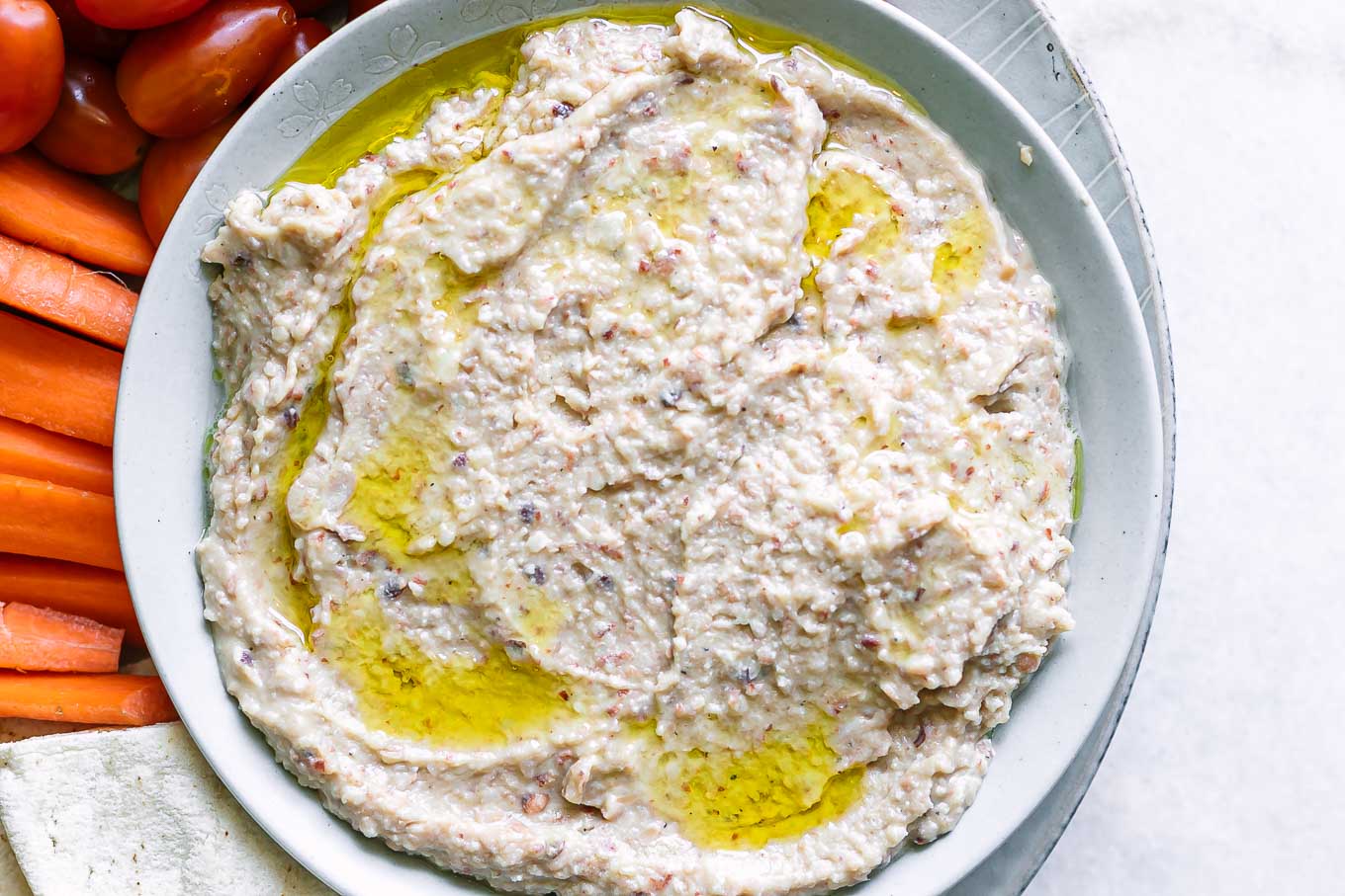 a bowl of black eyed pea hummus on a plate with cherry tomatoes, carrot sticks, and pita bread