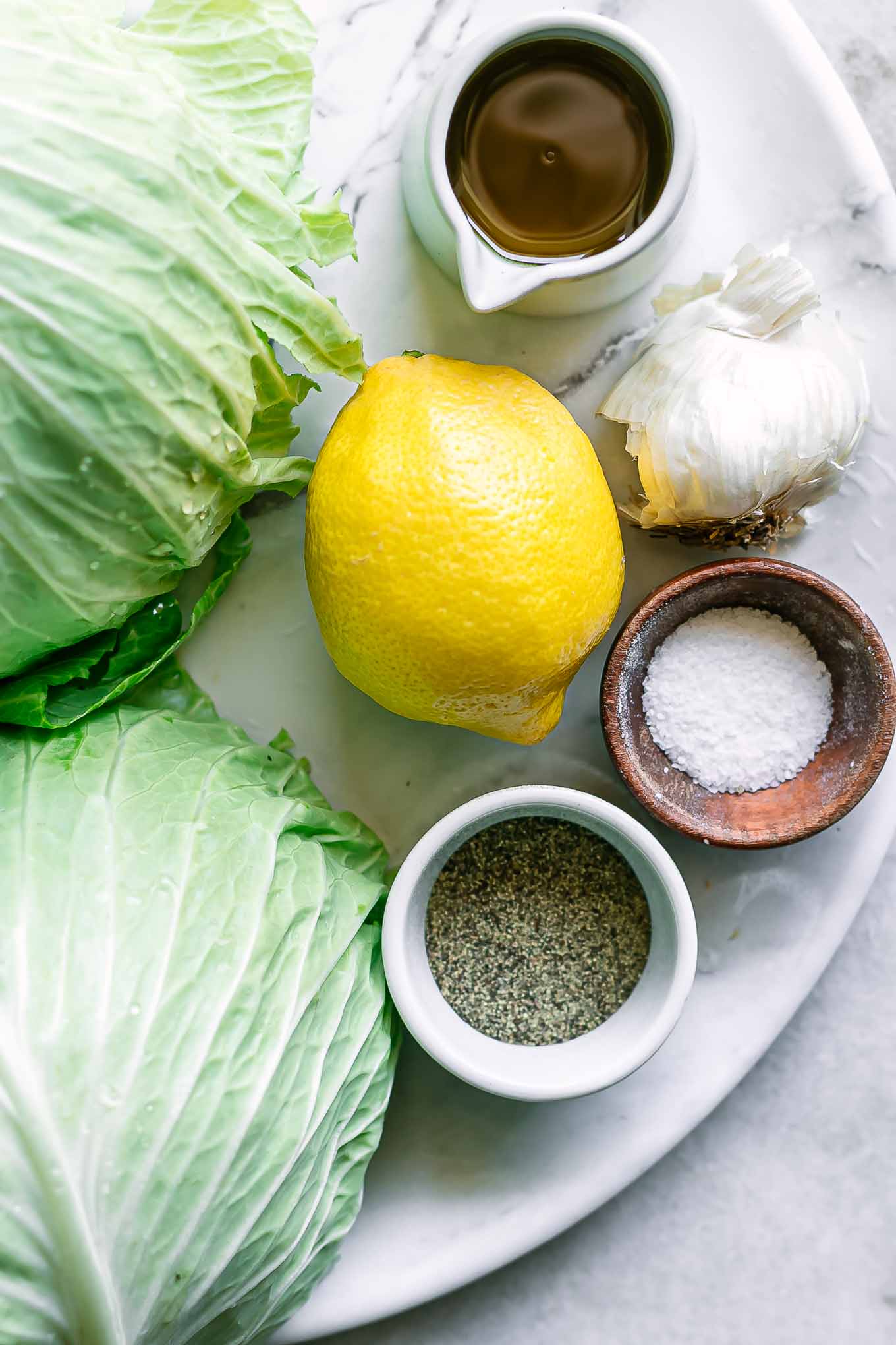 cabbage heads, lemon, olive oil, garlic, salt, and pepper on a table for baking cabbage crisps