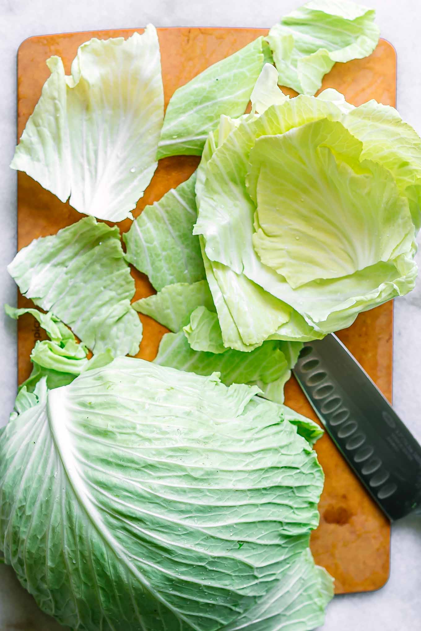 washed and cut cabbage leaves on a wood cutting board with a knife