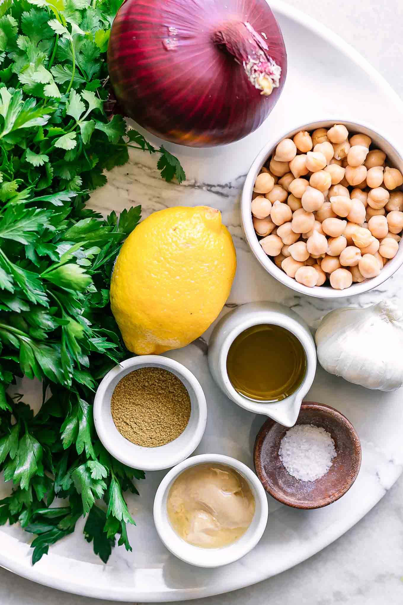 bowls of chickpeas, onion, lemon, spices, seasonings, and fresh herbs for falafel on a white table