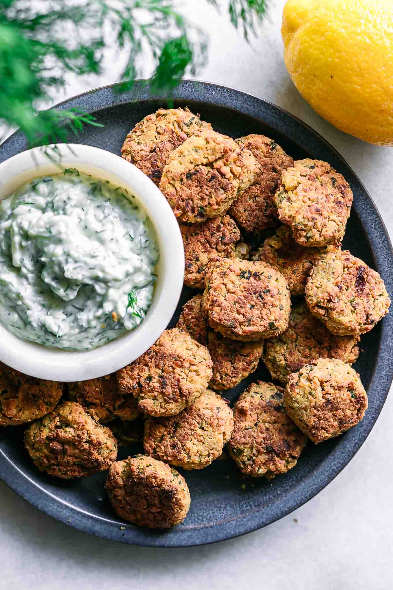 baked falafel balls on a blue plate with a white dip on a white table