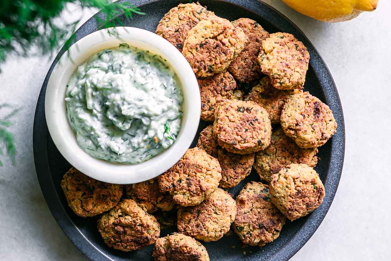 a blue plate with crispy baked falafel balls and a white dipping sauce on a white table