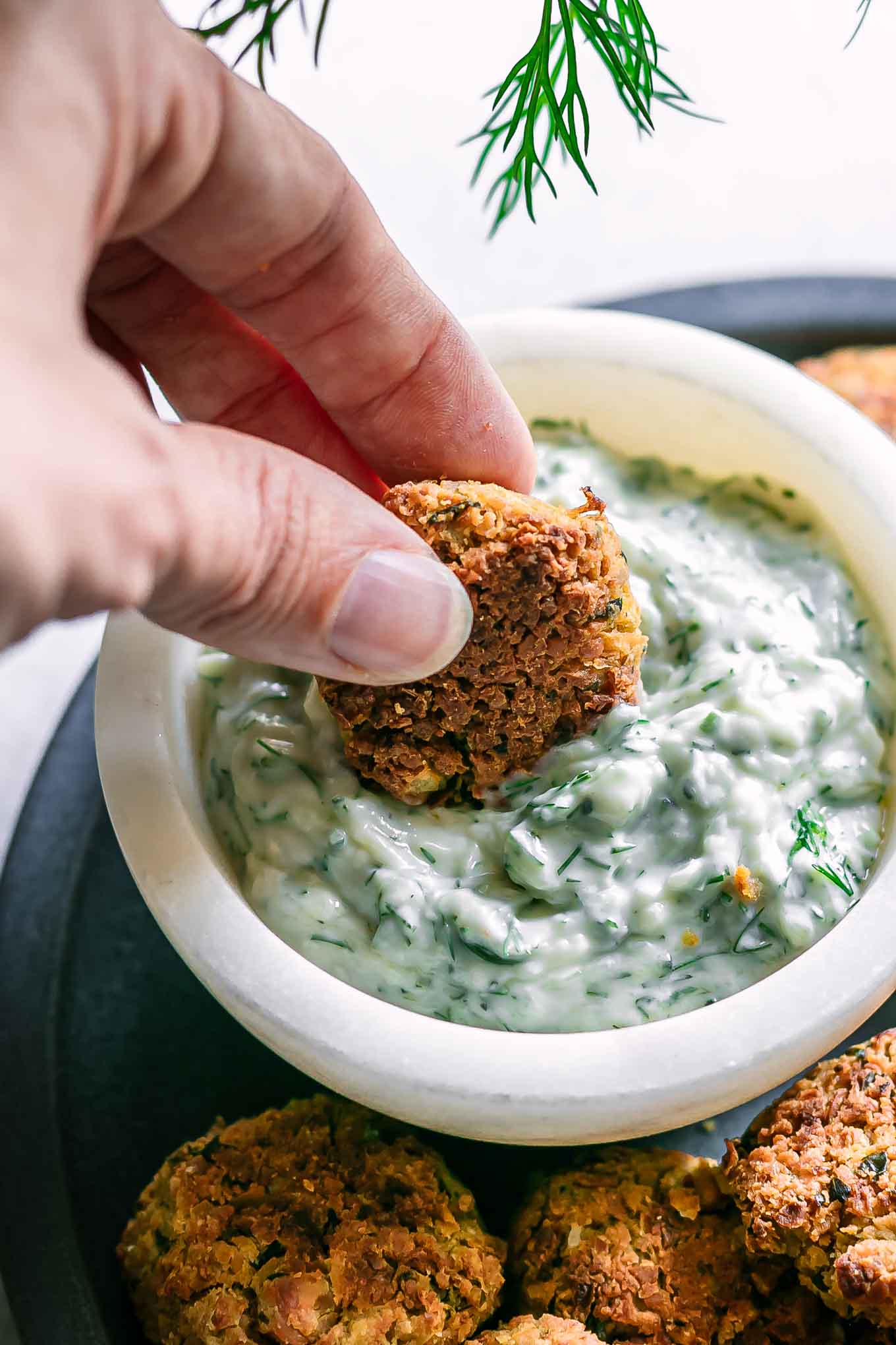 a hand dipping a falafel ball into tzatziki sauce on a blue plate
