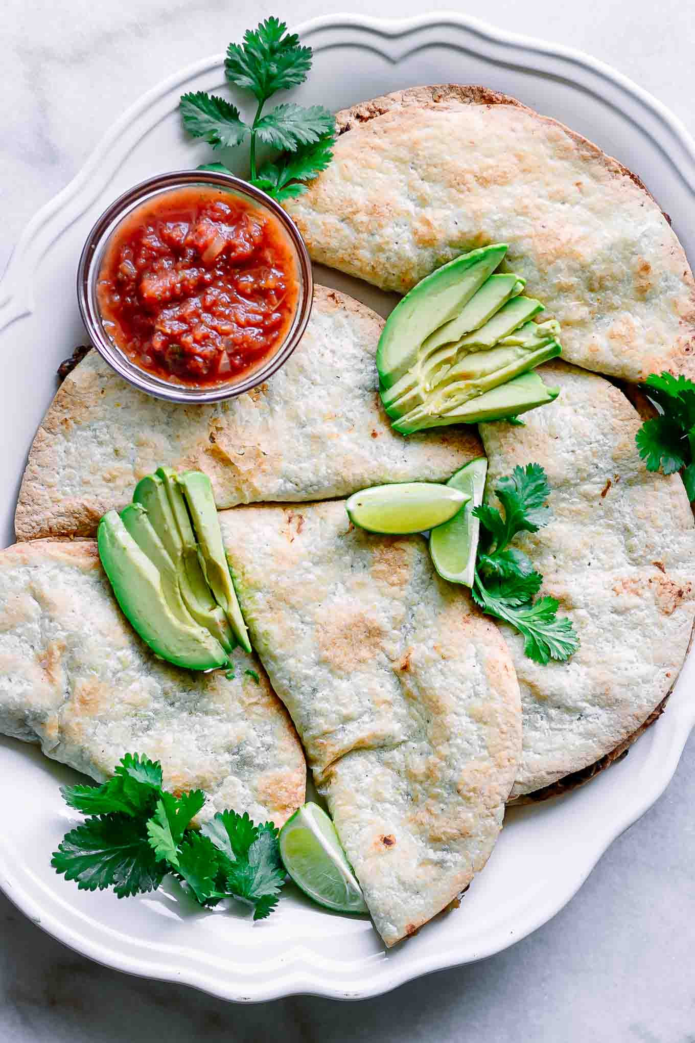 a white plate with crispy black bean tacos with a bowl of salsa and sliced avocados