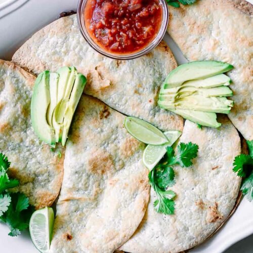 crispy baked black bean tacos on a white plate with avocados and salsa