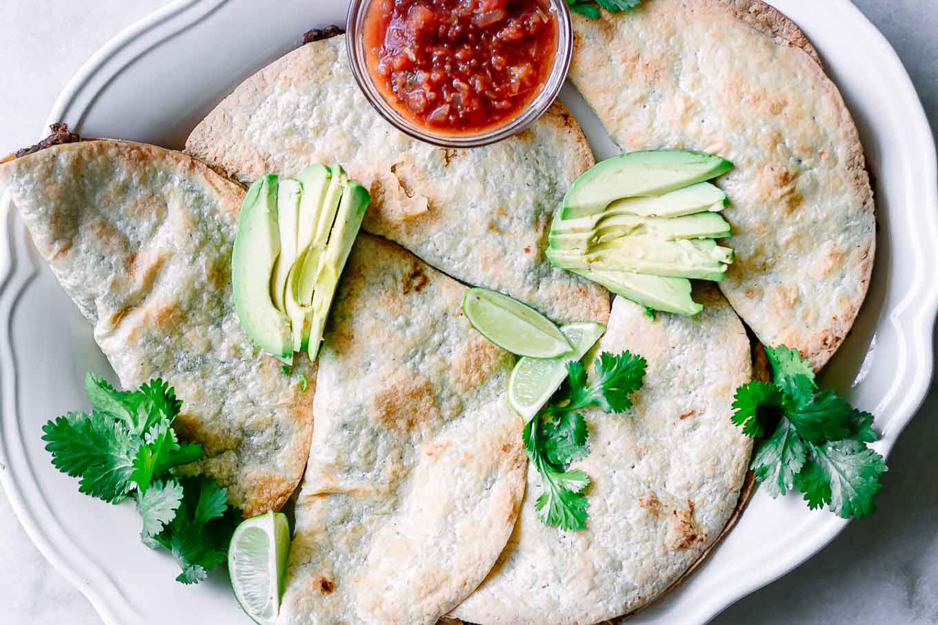 crispy baked black bean tacos on a white plate with avocados and salsa