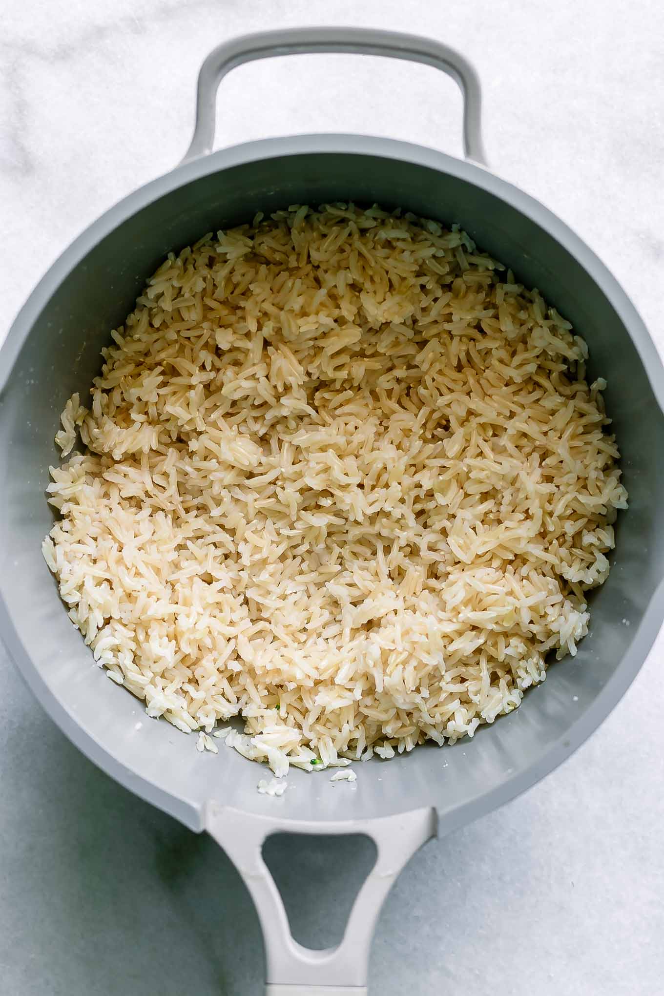 a small pot with cooked brown rice on a white table