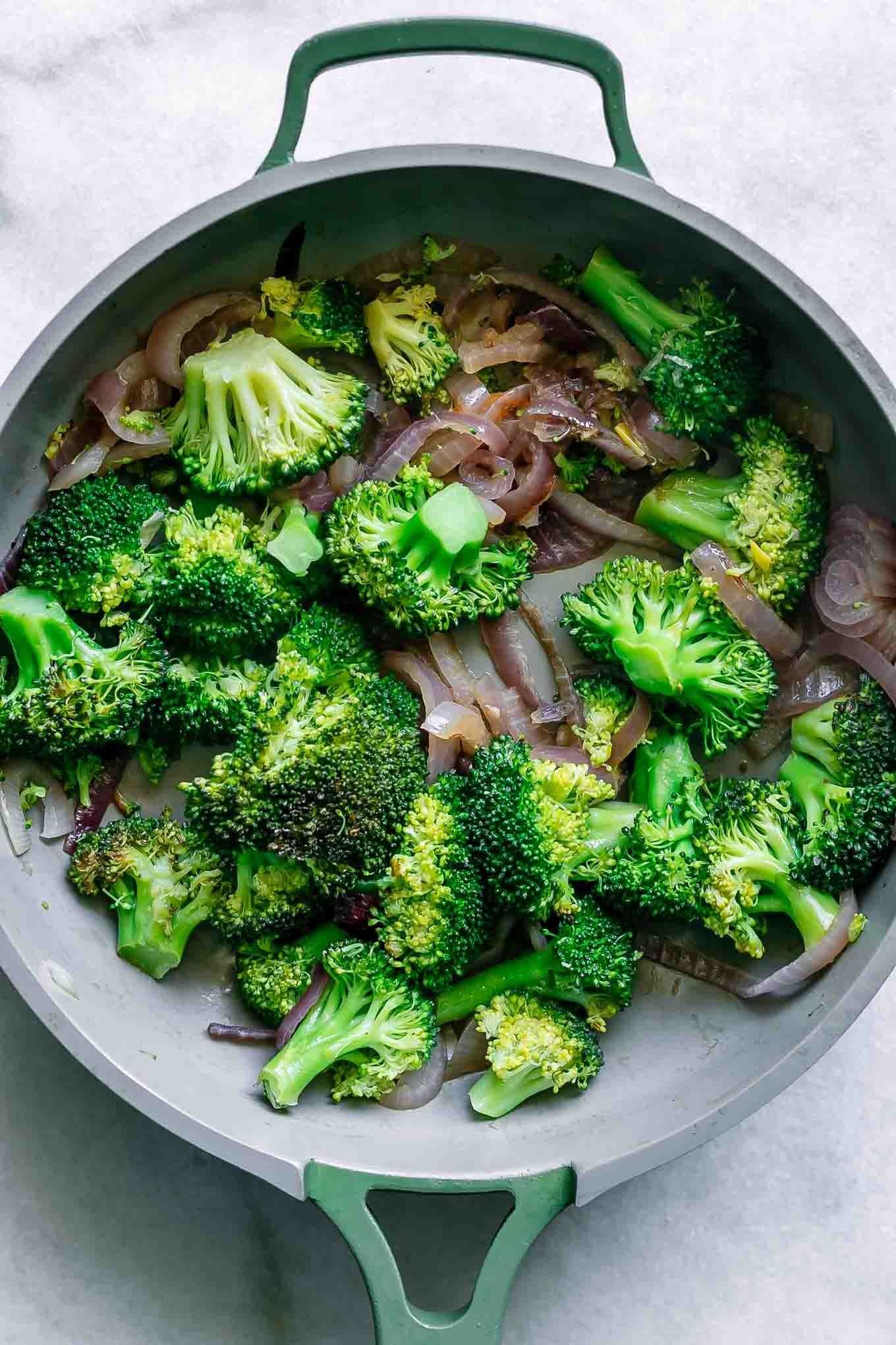 cooked broccoli and onions in a pan on a white table