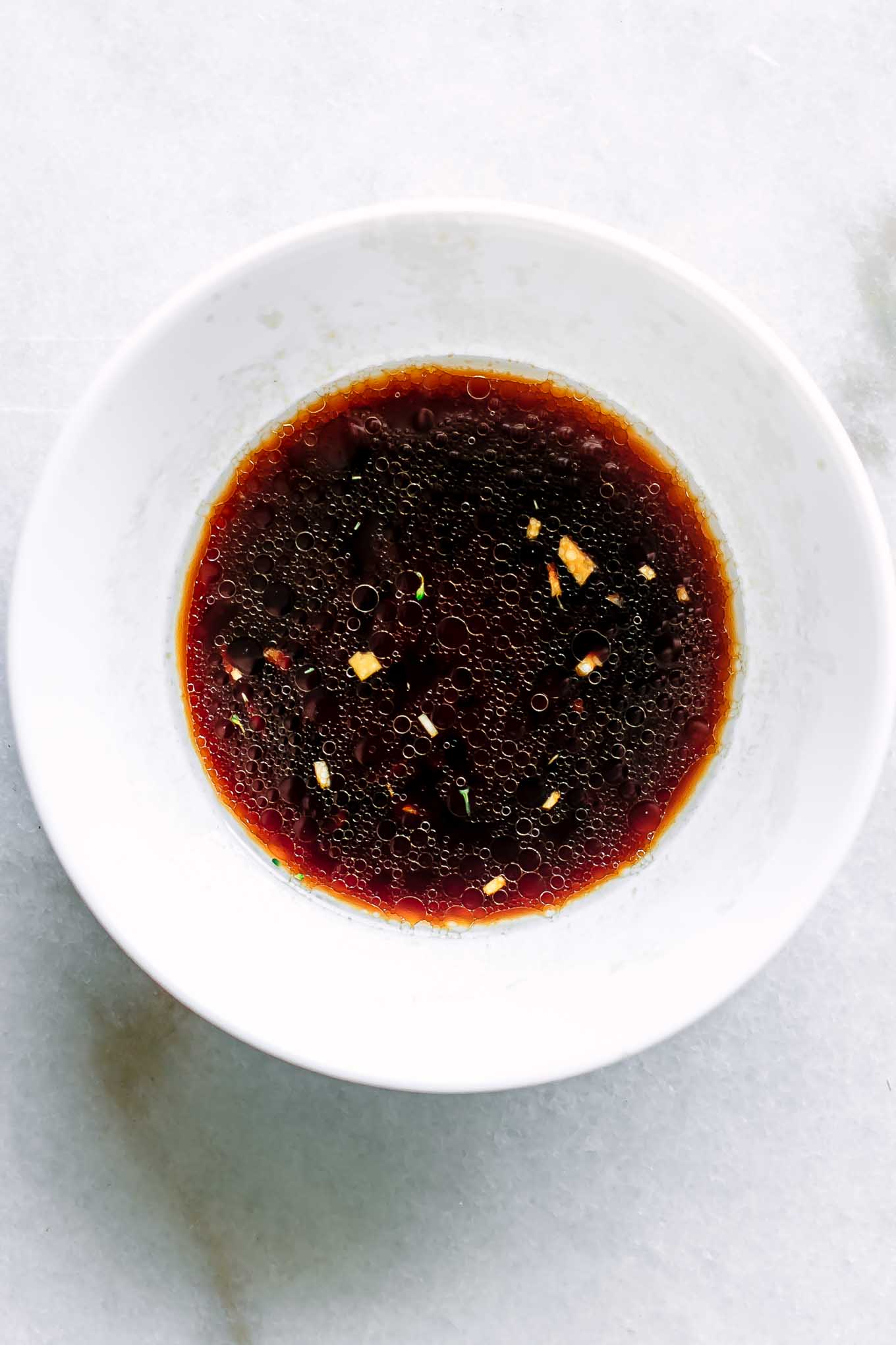 a white bowl with soy sauce, sesame oil, rice vinegar, ginger, and garlic on a white table