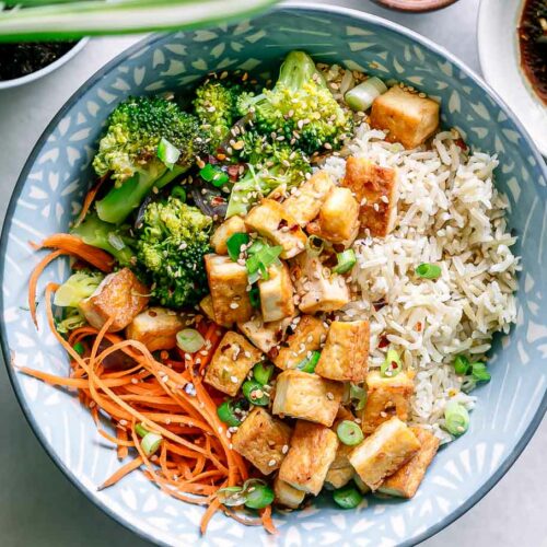 a bowl with brown rice, tofu, broccoli, carrots, and onions