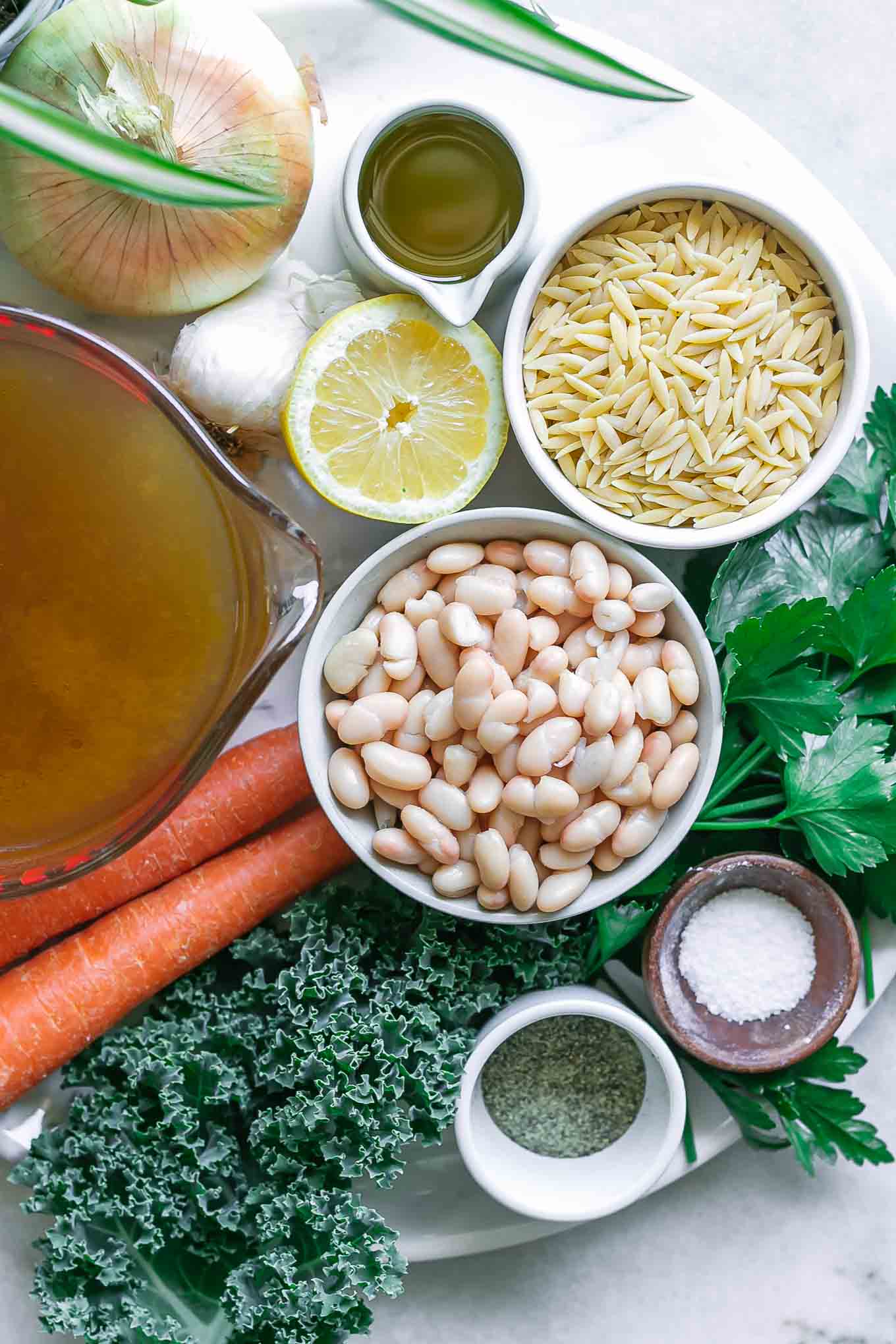 bowls of orzo, white beans, lemon, kale, oil, onion, kale, carrots, and broth for soup