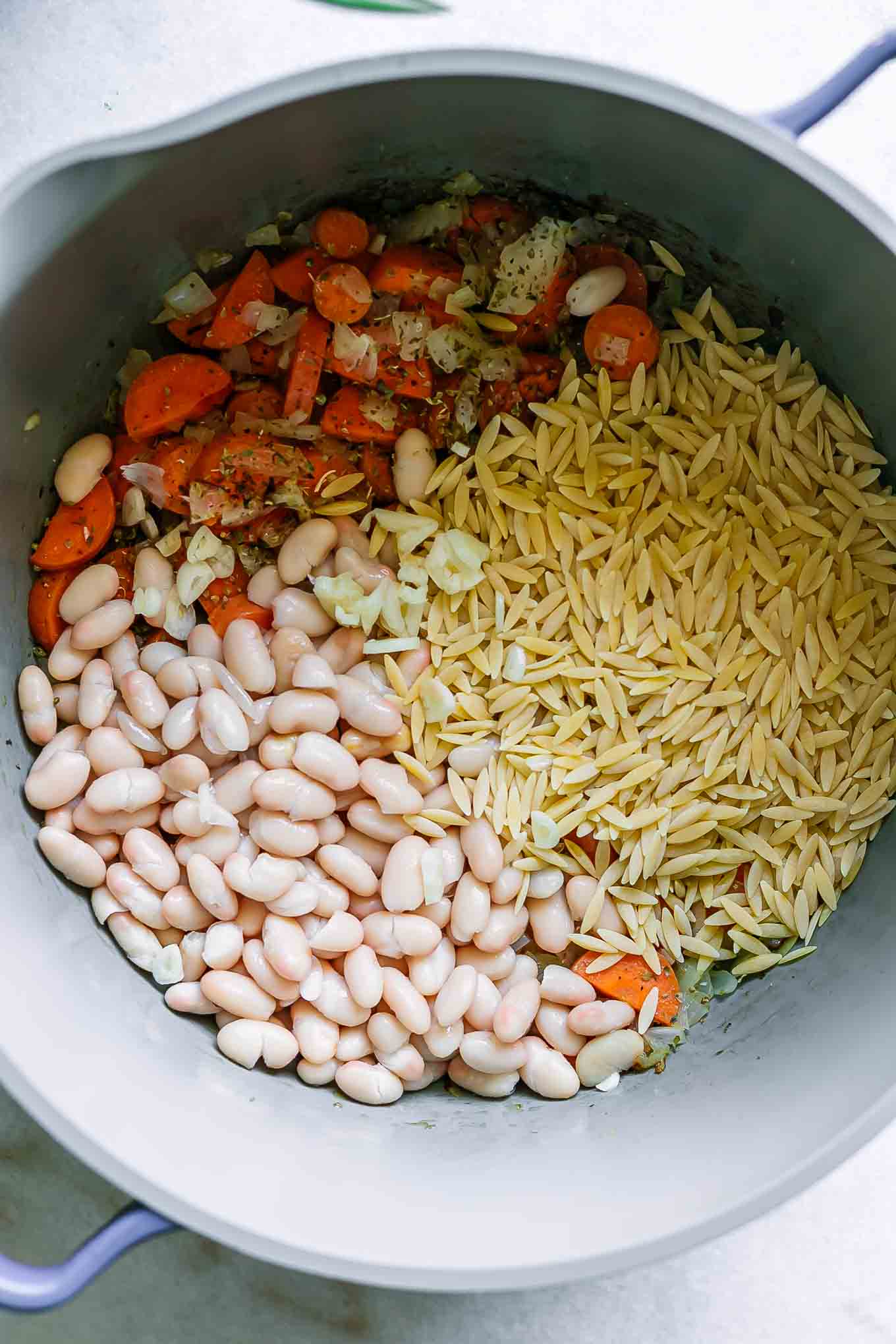 a pot with cooked vegetables, white beans, and orzo for soup