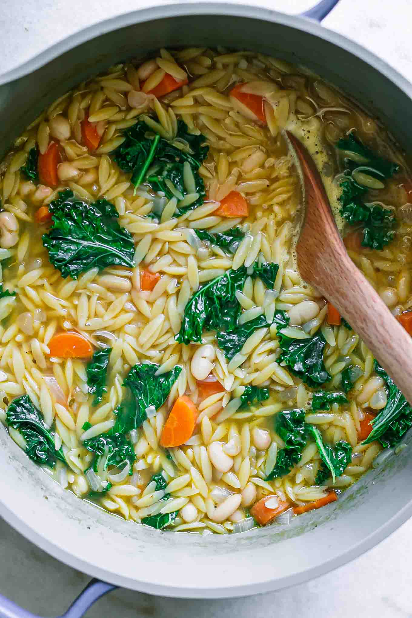a soup pot with simmering orzo and white bean soup with kale