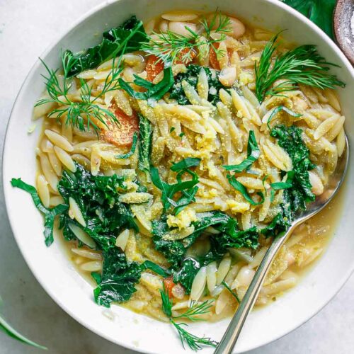 a bowl with lemon orzo soup with kale and lemon on a white table