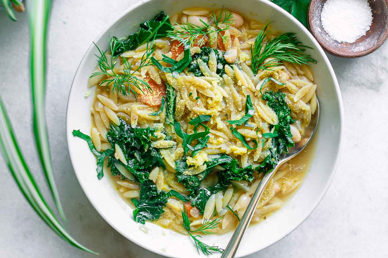 a bowl with lemon orzo soup with kale and lemon on a white table