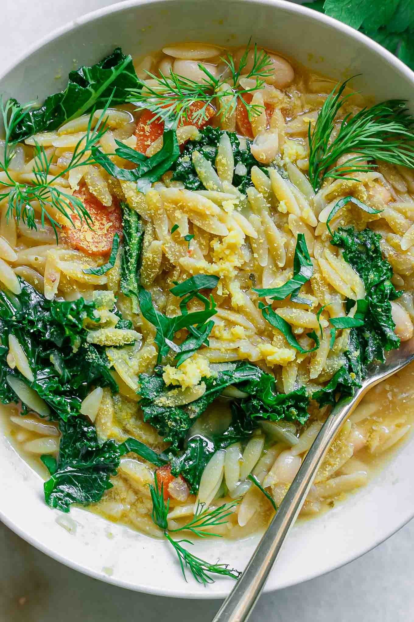 a close up photo of orzo lemon kale soup with white beans and fresh herbs