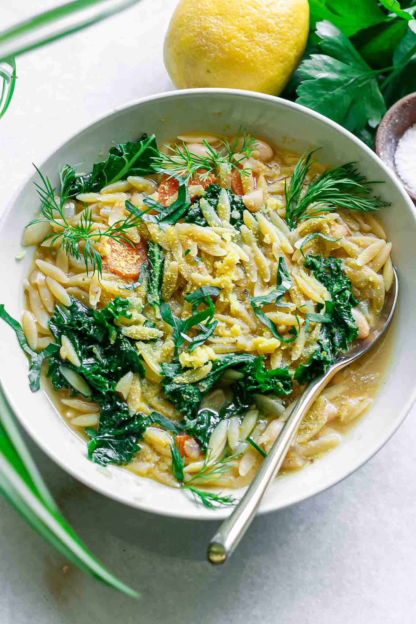 a bowl of lemon orzo white bean soup with kale in a white bowl with a gold fork